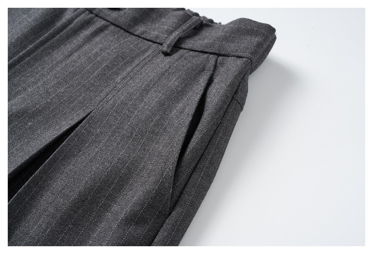 Close-up of charcoal gray trousers showing a belt loop, waistband, and front pleat.