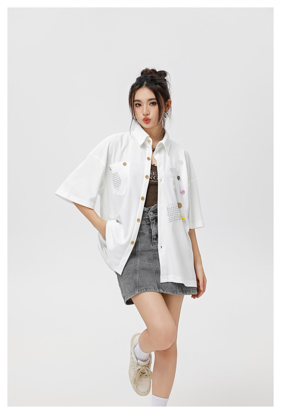 Model wearing the white short-sleeve button shirt open over a brown top with a gray denim skirt, three-quarter view