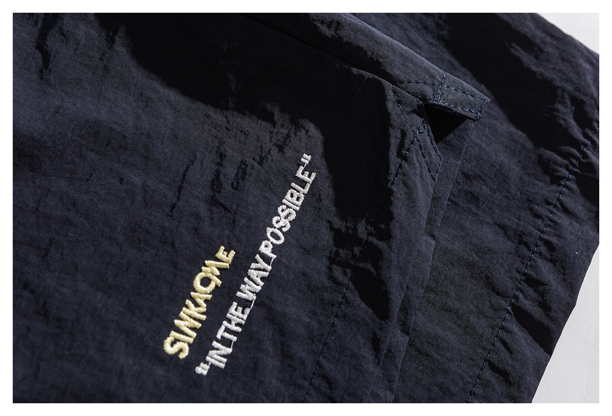 Close-up of gold and white embroidered English lettering beside a seam on dark shorts.