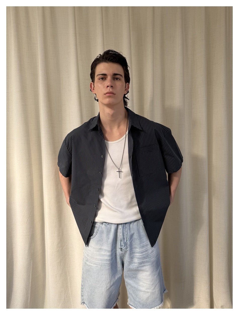 Closer front view of a model wearing a dark pinstriped short-sleeve shirt over a white tank and light blue denim shorts.