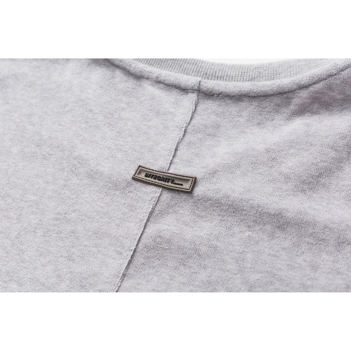 Close-up of a small metal INTEGRITY badge on heather-gray fabric.