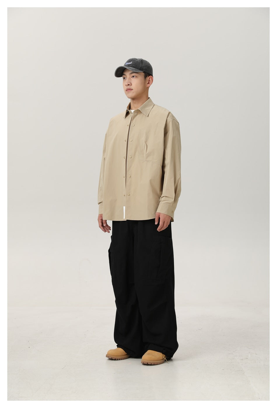 Model wearing a khaki button-up shirt with black wide-leg cargo pants, a gray cap and tan boots, seen from the side