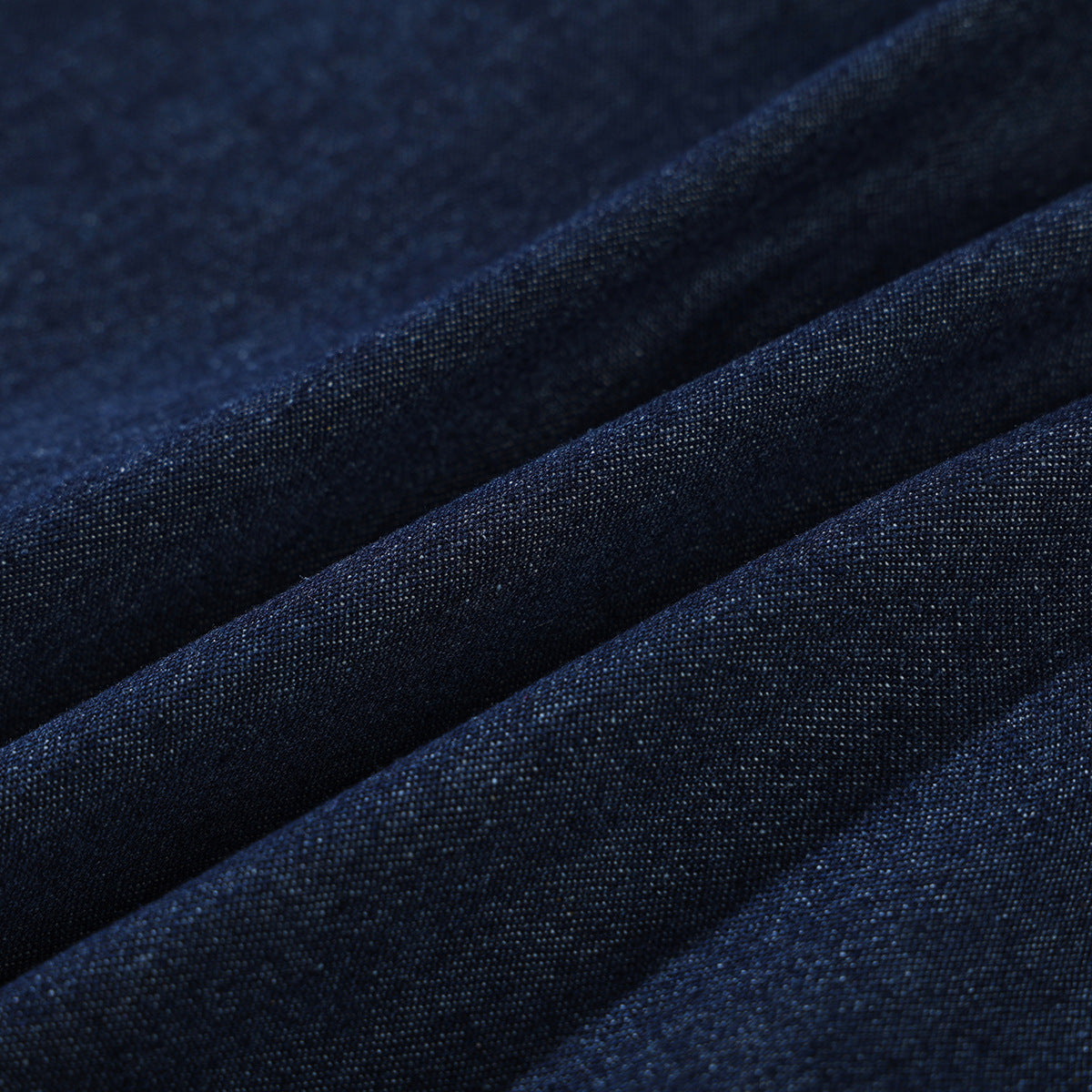 Macro view of dark indigo denim fabric gathered into folds.