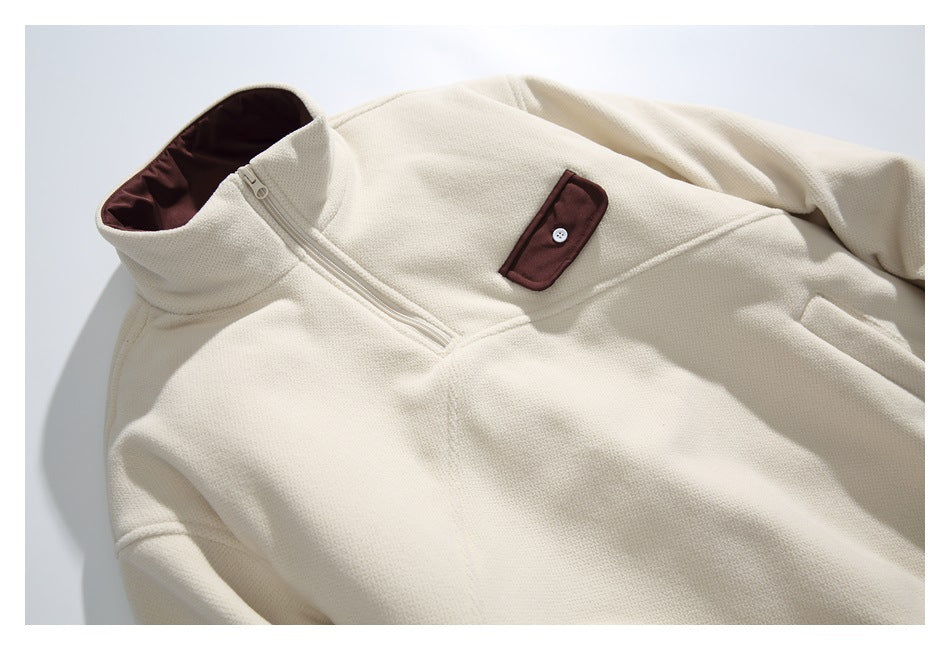 Close-up of an ivory quarter-zip pullover showing its zipper, raised collar, and burgundy buttoned chest pocket.