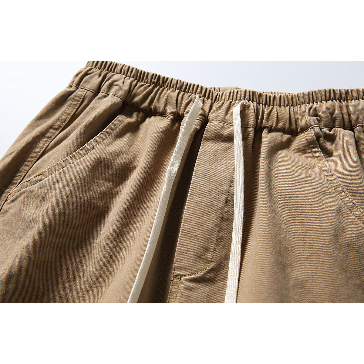 Close-up of tan trousers showing an elastic waistband, white drawstrings, and angled front pockets.