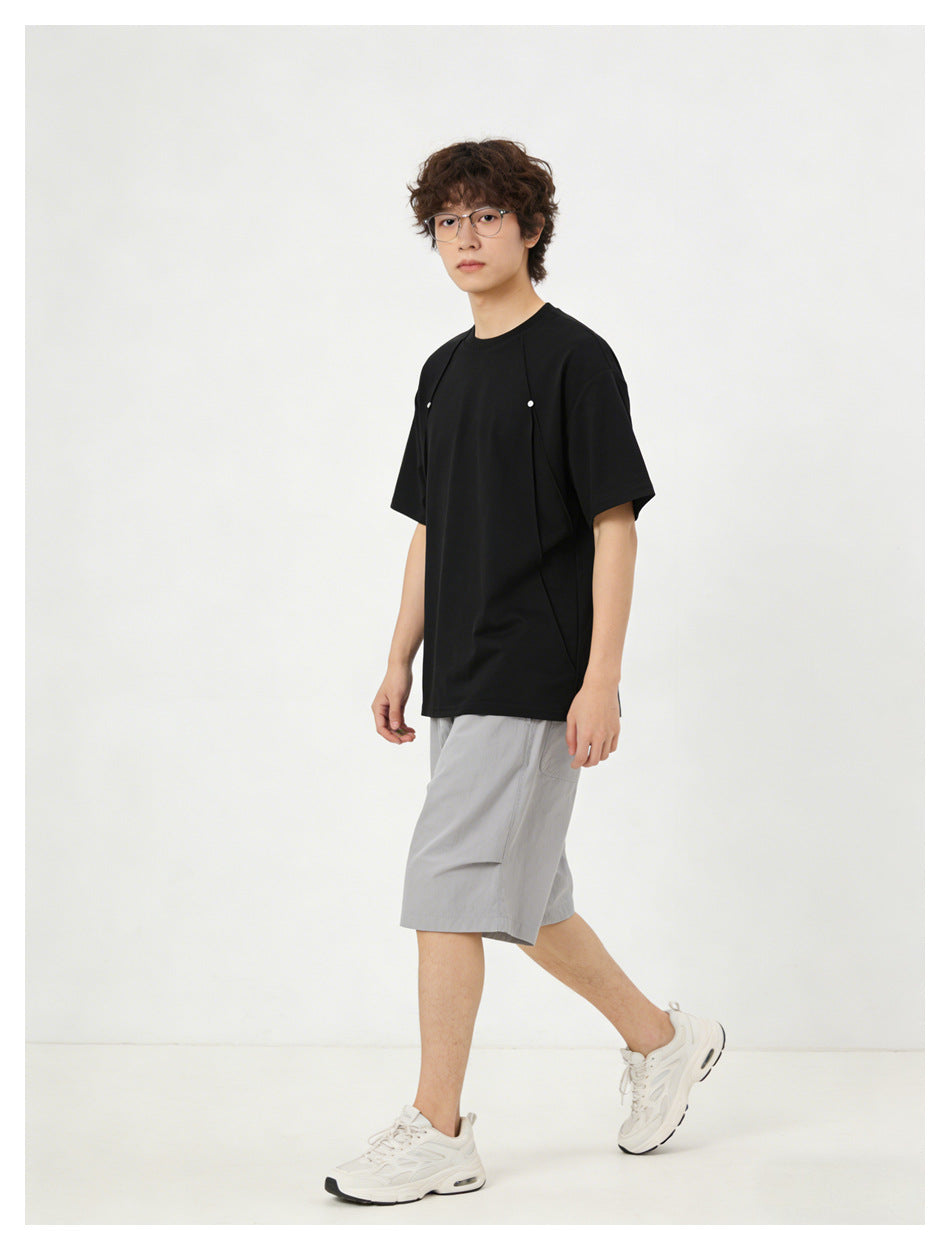 Angled view of a model in a black short-sleeve shirt with shoulder details and light gray shorts.