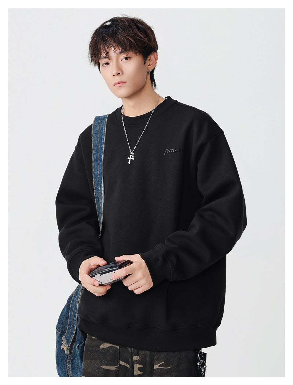 Model wearing a black oversized crewneck sweatshirt with a small embroidered chest mark, holding a compact camera.