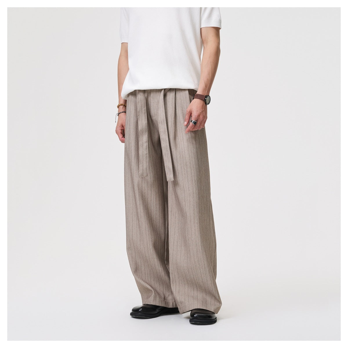 Model in loose khaki pinstriped wide-leg trousers with hanging tie belt, white tee and black shoes, angled view