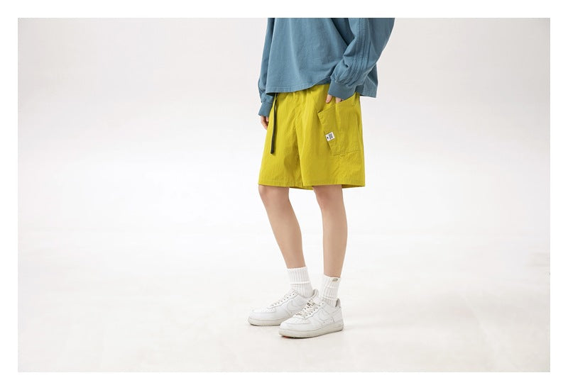 Cropped angled view of a model wearing bright yellow shorts with a blue long-sleeve shirt and white sneakers.