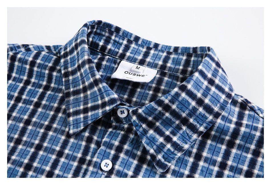 Close-up of a blue, black, and white plaid shirt collar, front buttons, and neck label.