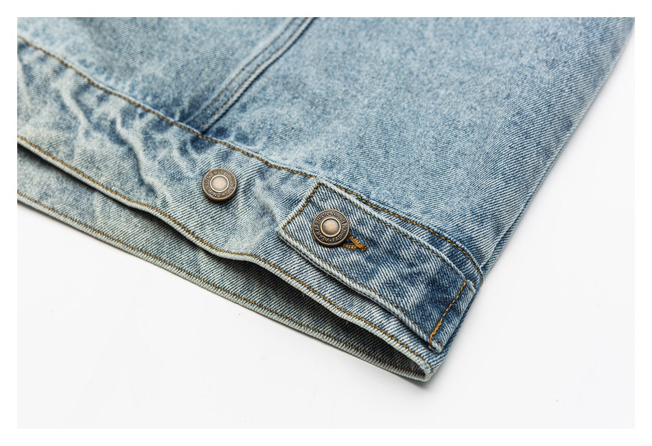 Close-up of a light blue denim jacket hem with metal buttons and a buttoned adjustment tab.