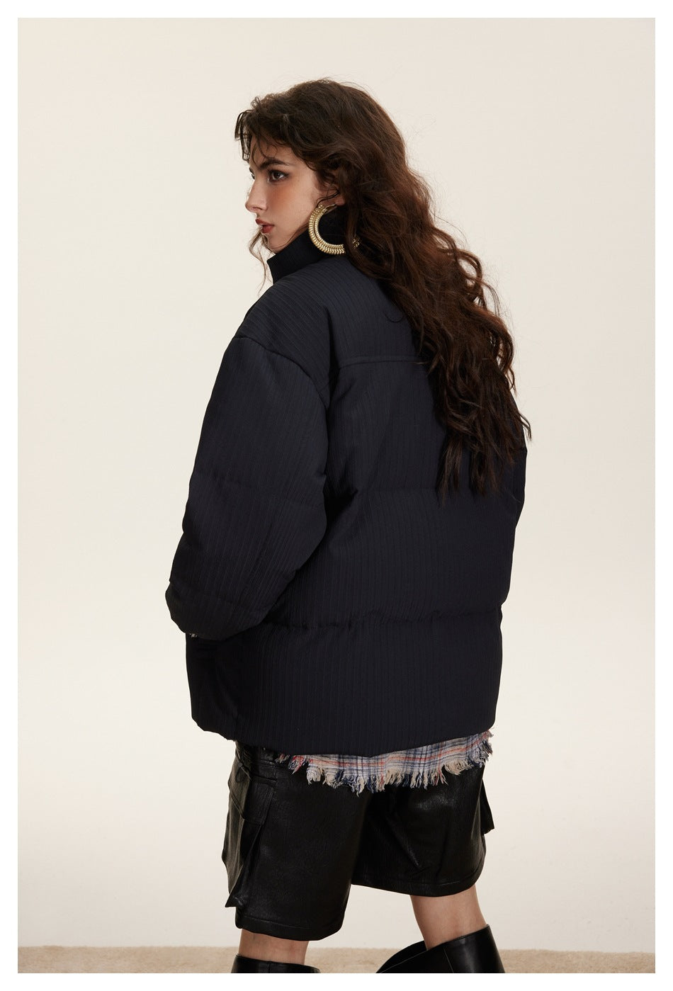 Model turned away to show the back of a dark navy padded jacket with a high collar and dropped shoulders.