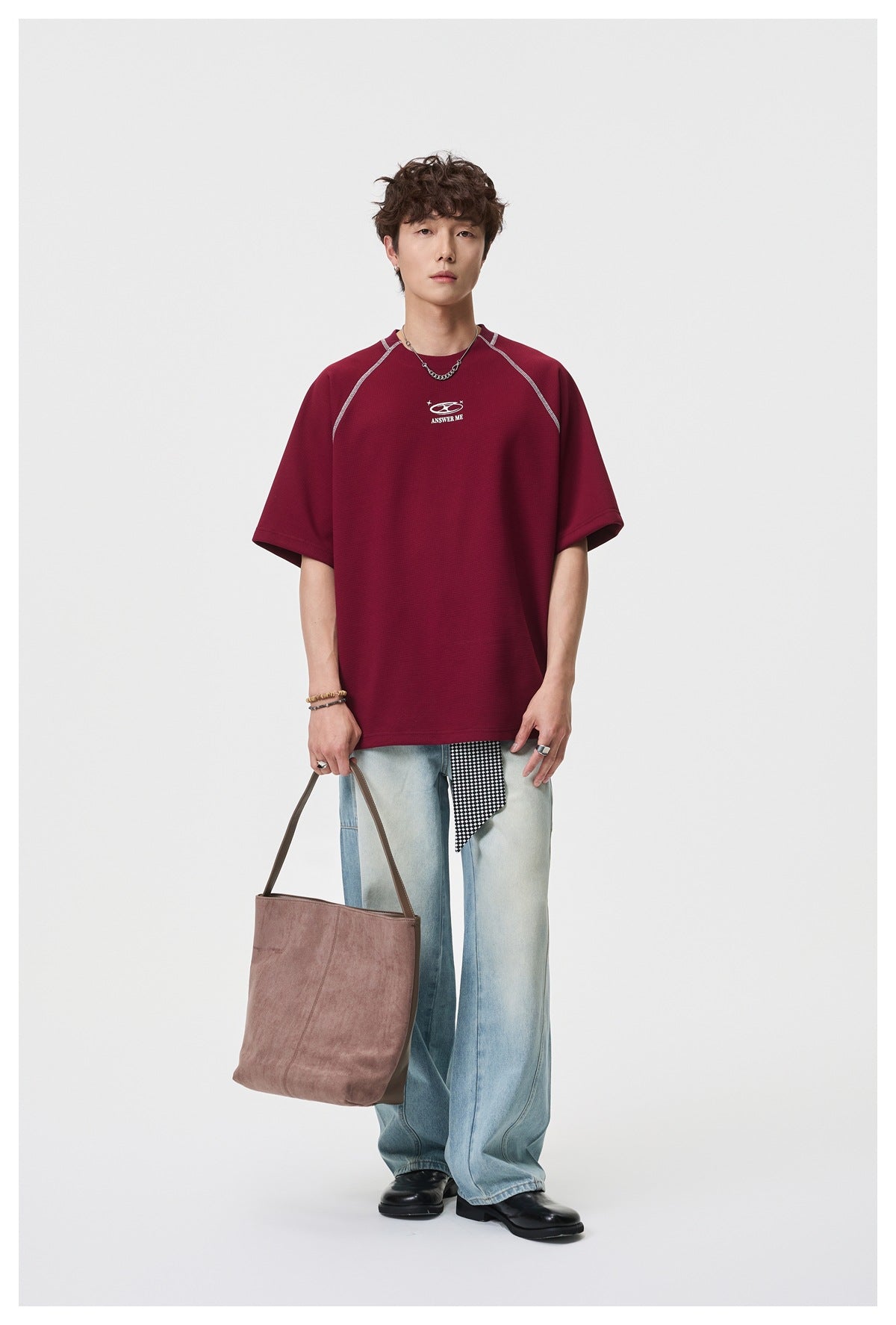 Full-length model wearing an oversized burgundy short-sleeve shirt with contrast seams and a small chest graphic.