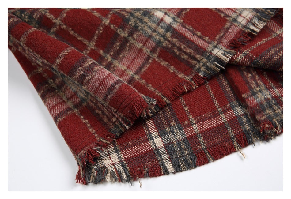 Close-up of red, charcoal, and cream plaid fabric with a fringed edge on a white background.