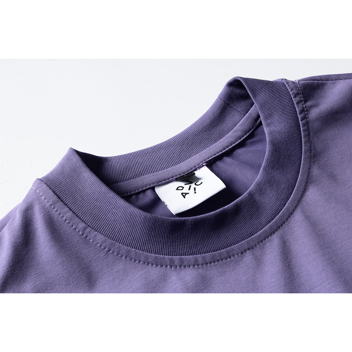 Close-up of a purple T-shirt's ribbed crew neck, stitching, and inner label.