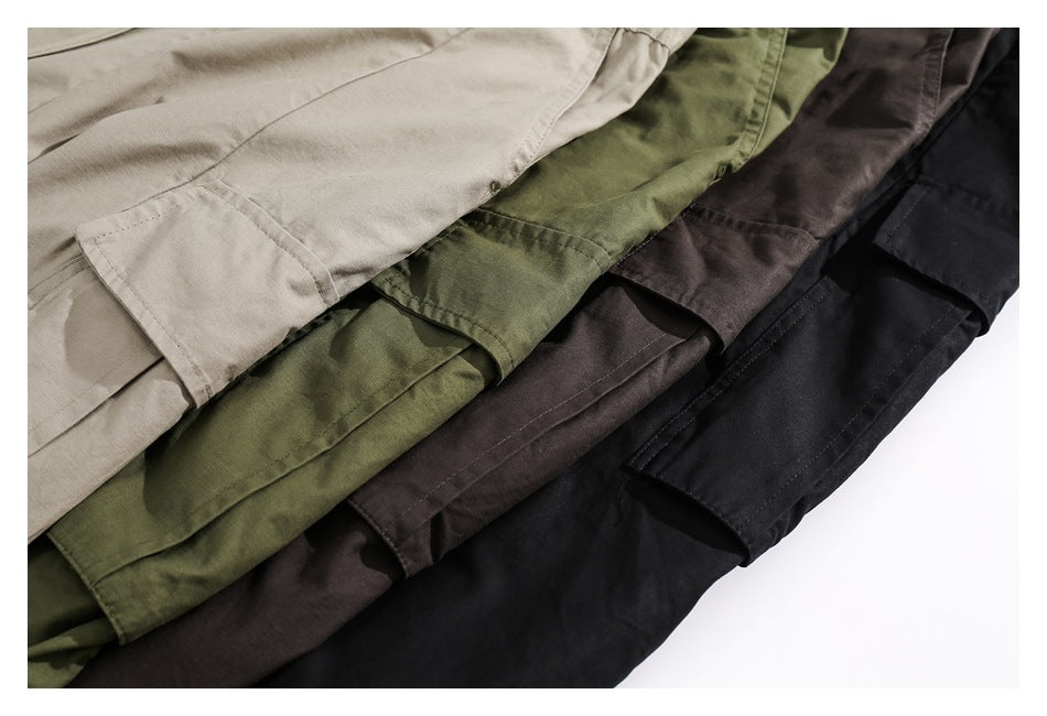 Close-up of cargo pocket flaps on beige, olive, brown, and black pants arranged together.