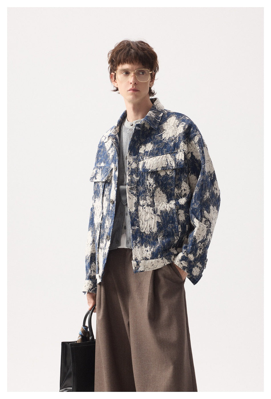 Model wearing a blue and cream floral-patterned button jacket over a gray cardigan and brown trousers.