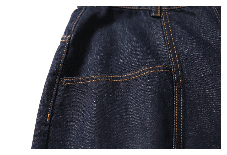 Close-up of a front pocket and orange-stitched seams on dark indigo jeans.