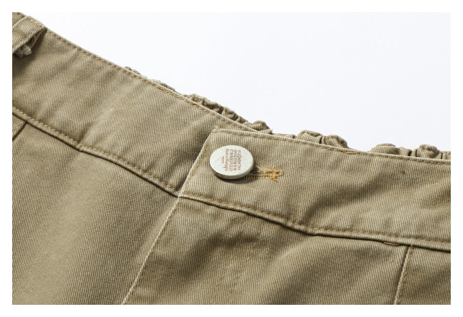 Close-up of the tan pants waistband and a round button, with stitching and gathered fabric visible.