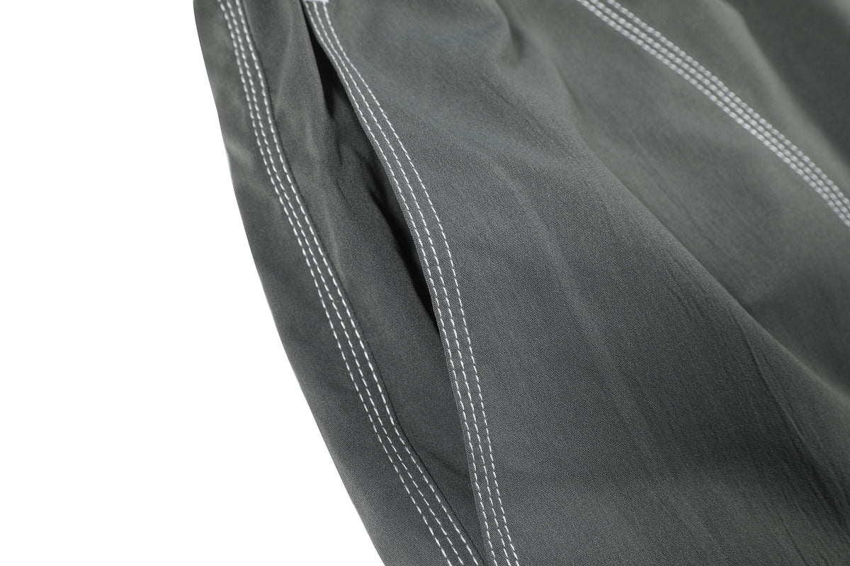 Close-up of a seam and pocket opening with parallel white topstitching on charcoal gray pants.