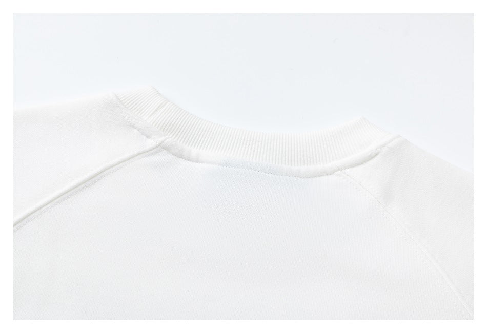Close-up of a white sweatshirt's ribbed crew neckline and raglan shoulder seams.