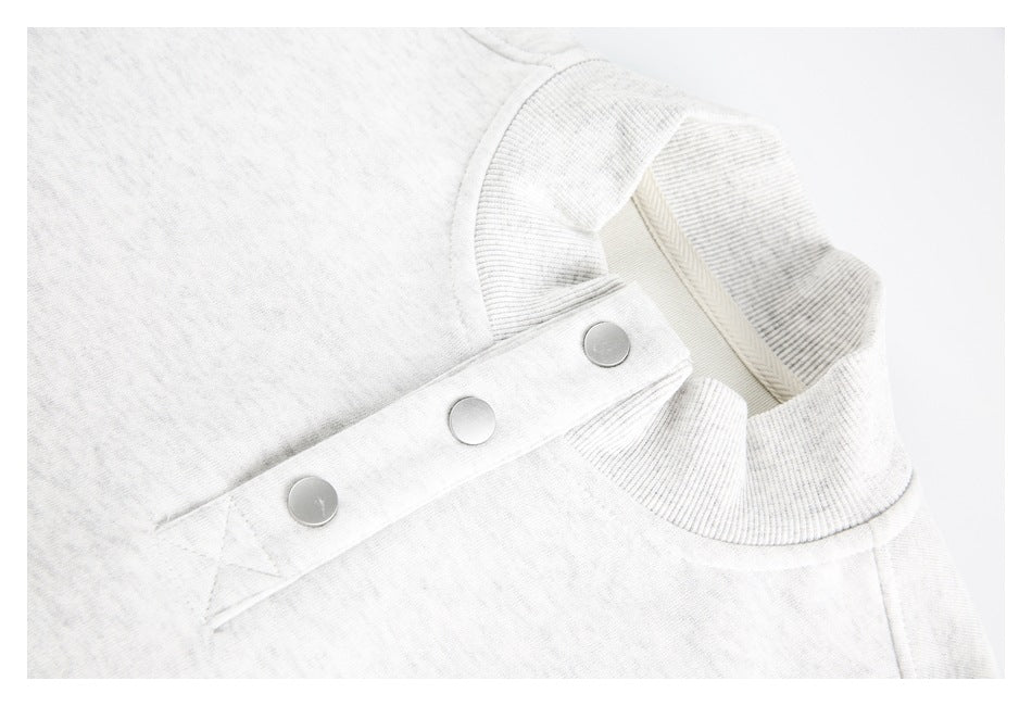 Close-up of a light heather gray ribbed neckline and a fabric tab with three silver snaps.