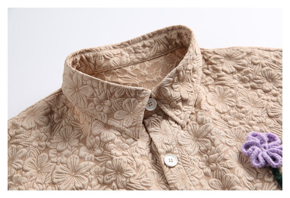 Close-up of a beige floral-textured shirt collar and white buttons.