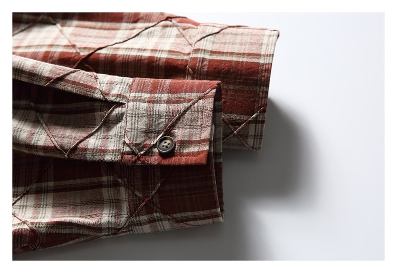 Close-up of a reddish-brown, cream, and gray plaid shirt cuff with a button and diagonal stitched detailing.