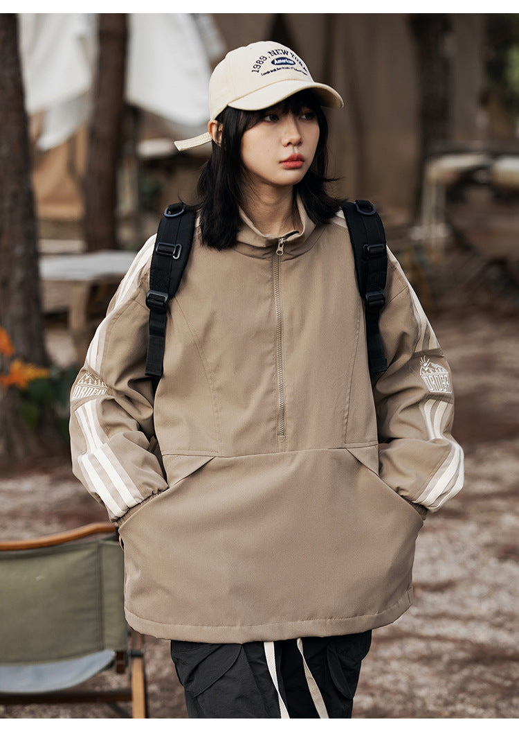 Front view of a model wearing a taupe pullover jacket with a short zipper, kangaroo pocket, cream sleeve stripes, and