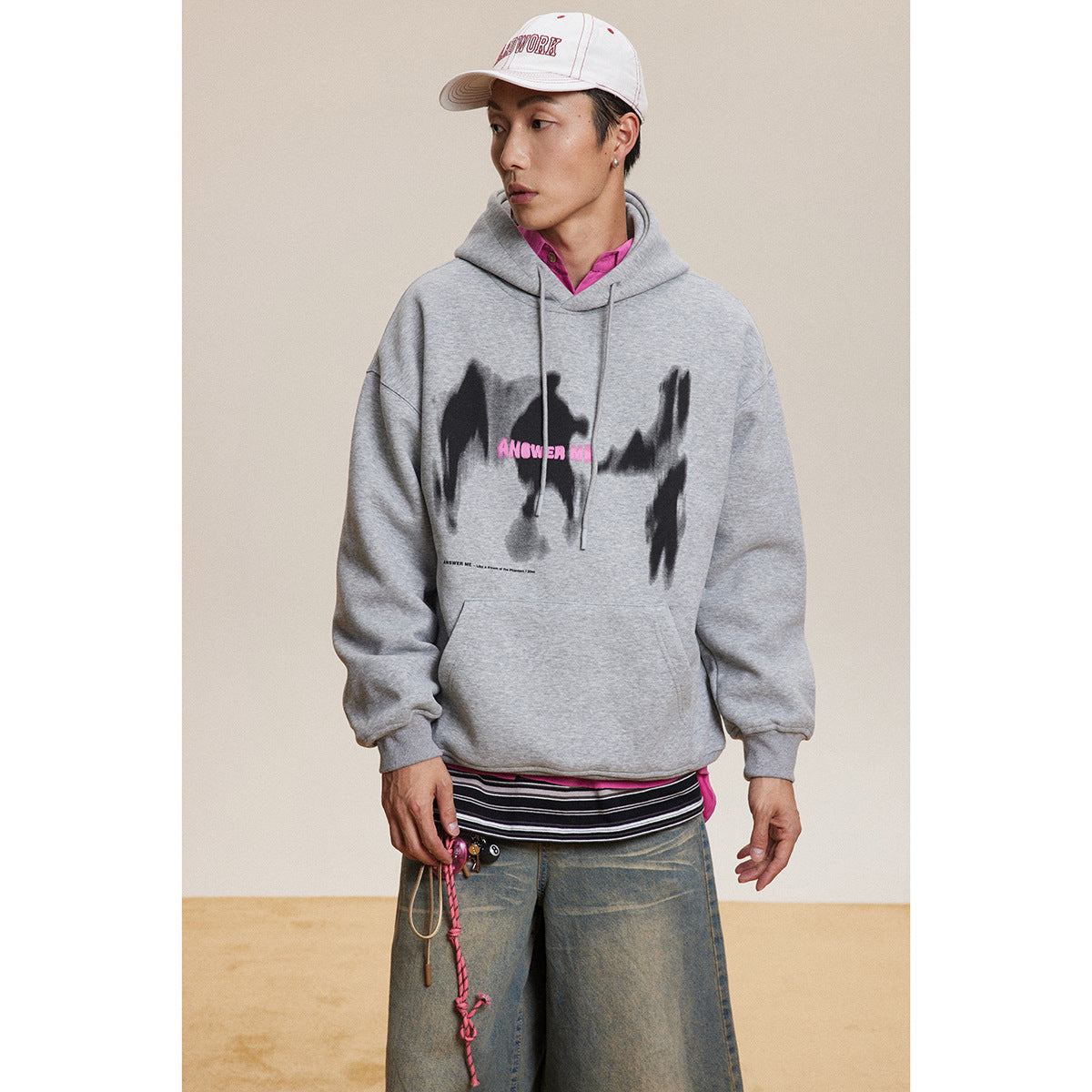 Model wearing a light gray hoodie with a black abstract chest graphic and pink lettering.