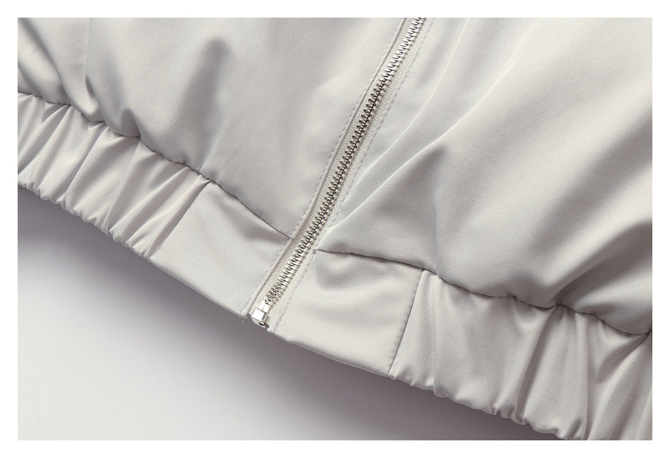 Close-up of a light gray jacket's front zipper and gathered elastic hem.