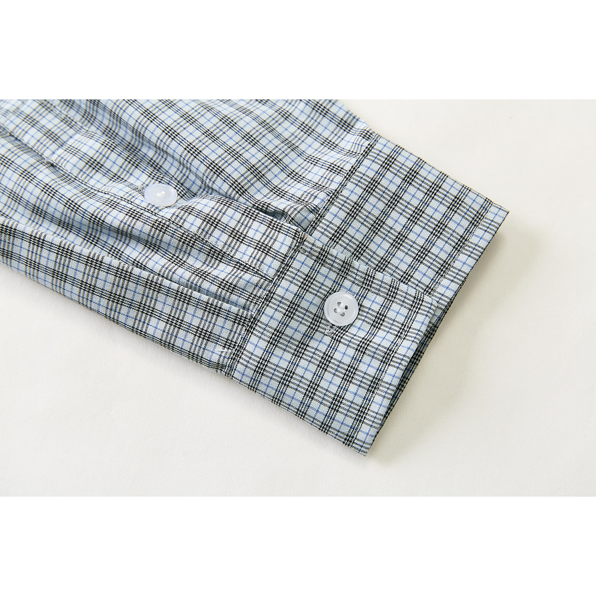 Close-up of a light blue, white, and dark checked shirt cuff with two white buttons.
