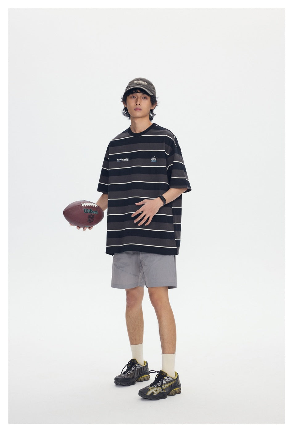 Model wearing a black and charcoal striped T-shirt and gray shorts, holding a football.