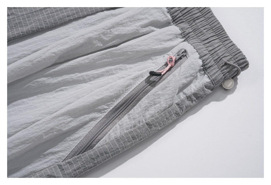 Close-up of a gray zip pocket with a pink pull cord beside the gathered waistband and contrasting grid-patterned panels.