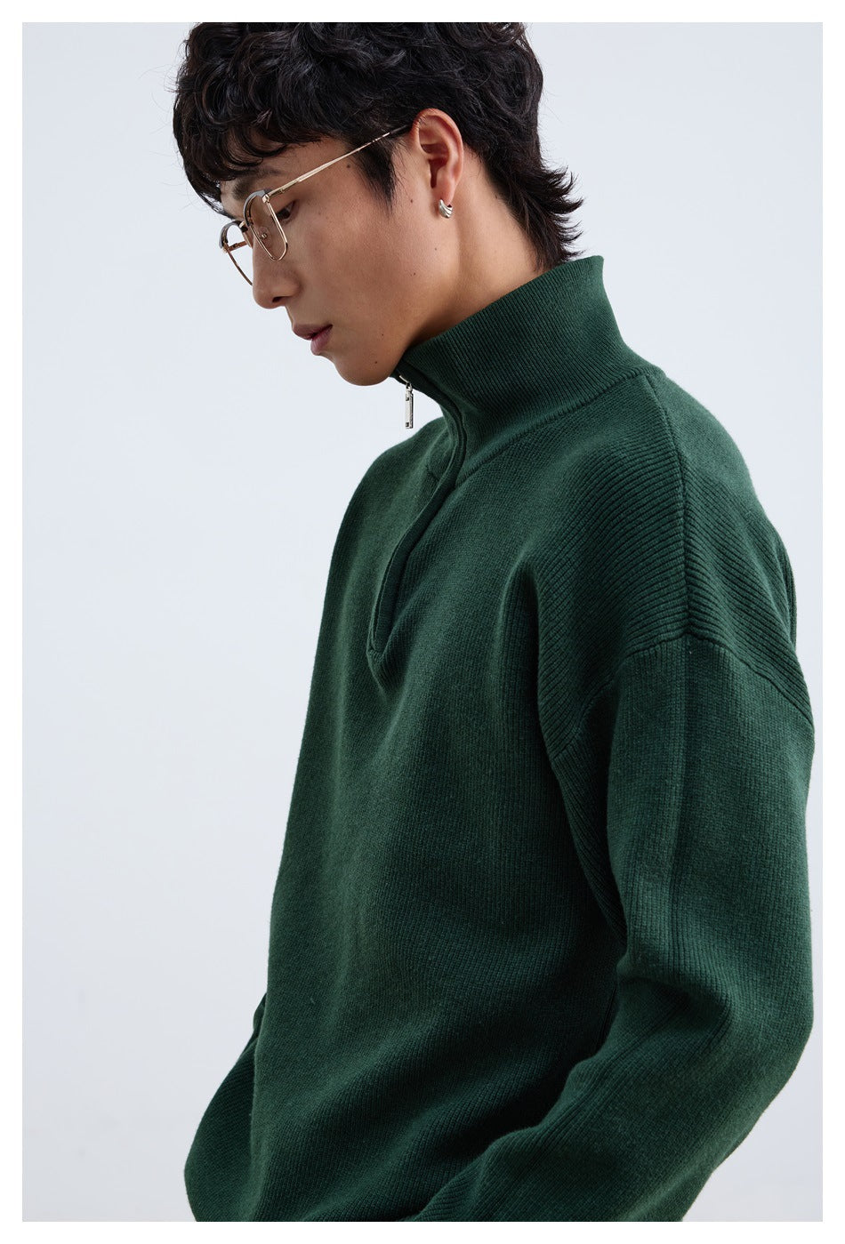 Close side view of a model wearing a dark green ribbed quarter-zip sweater with a tall collar.