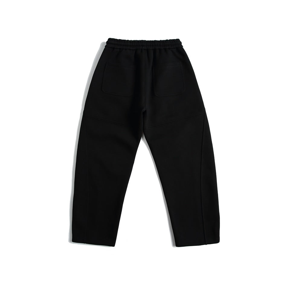 Back view of black jogger pants with an elastic waistband, two patch pockets, and stitched leg panels.