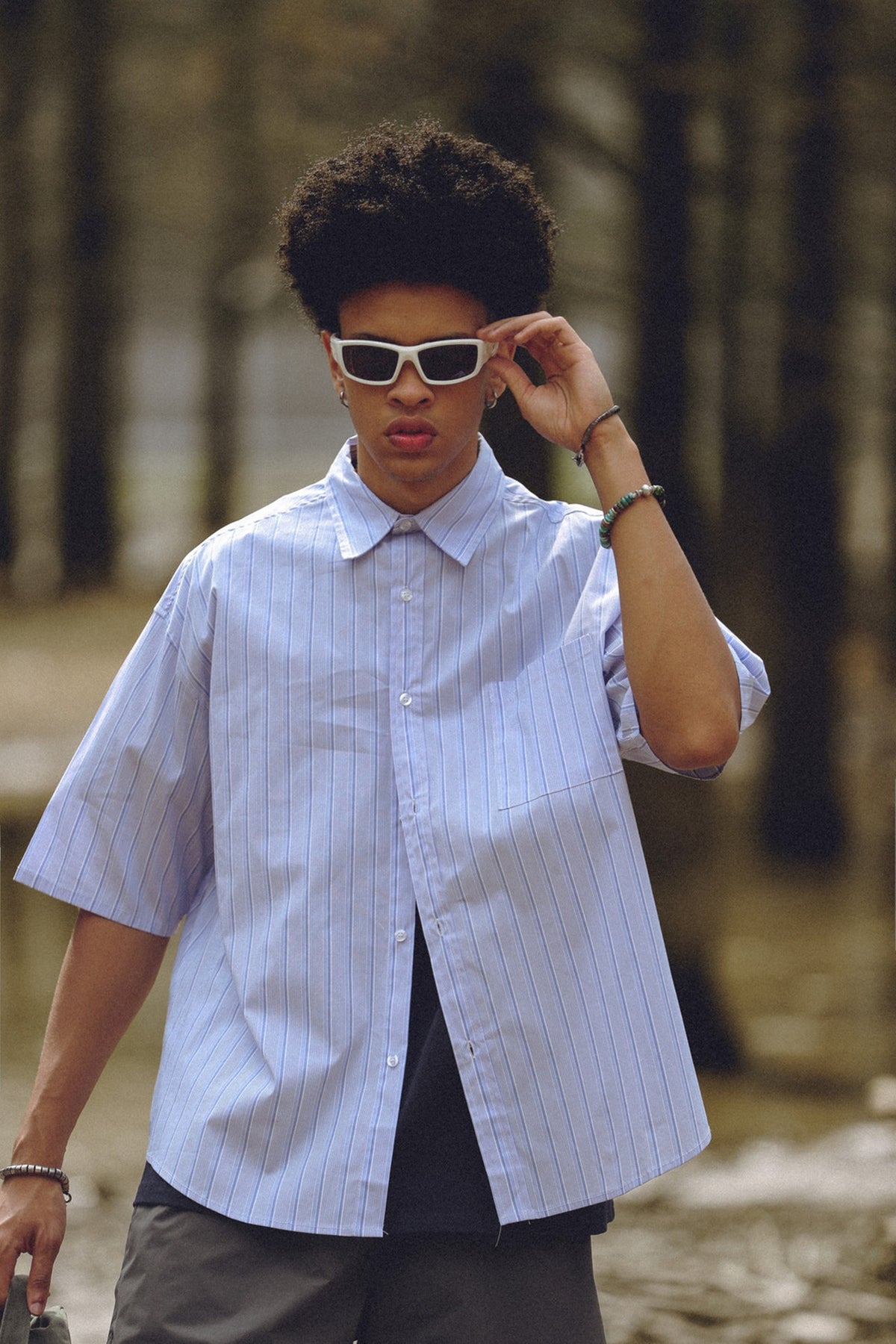 Closer view of a model wearing an oversized pale blue pinstriped short-sleeve button-up shirt with a chest pocket.