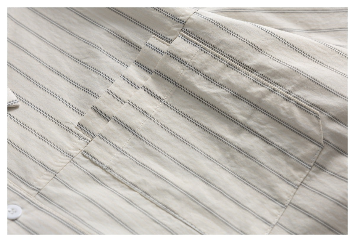 Close-up of an ivory shirt with fine dark stripes, showing a chest pocket and a white button.