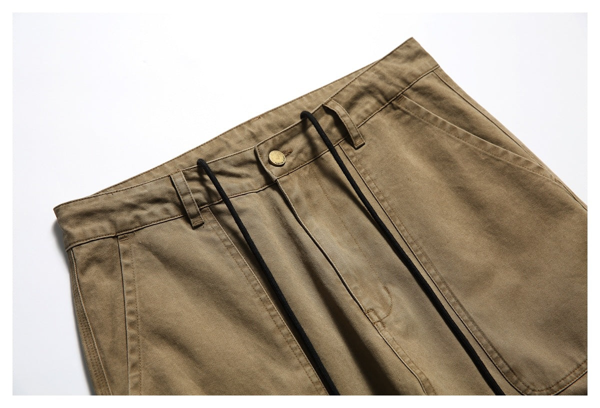 Close-up of the front waistband and upper section of tan-brown trousers with belt loops, a brass button and black