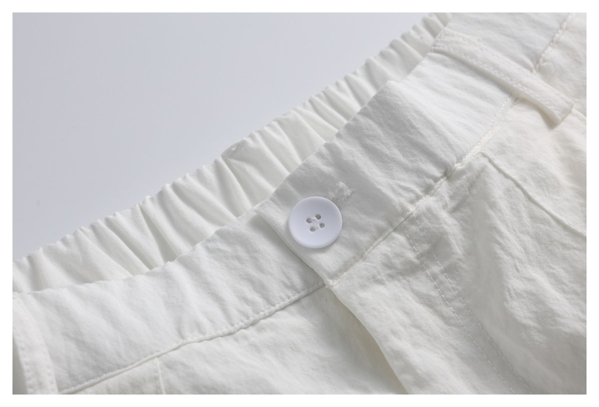Close-up of an off-white trouser waistband with gathered elastic, a white button and belt loop.