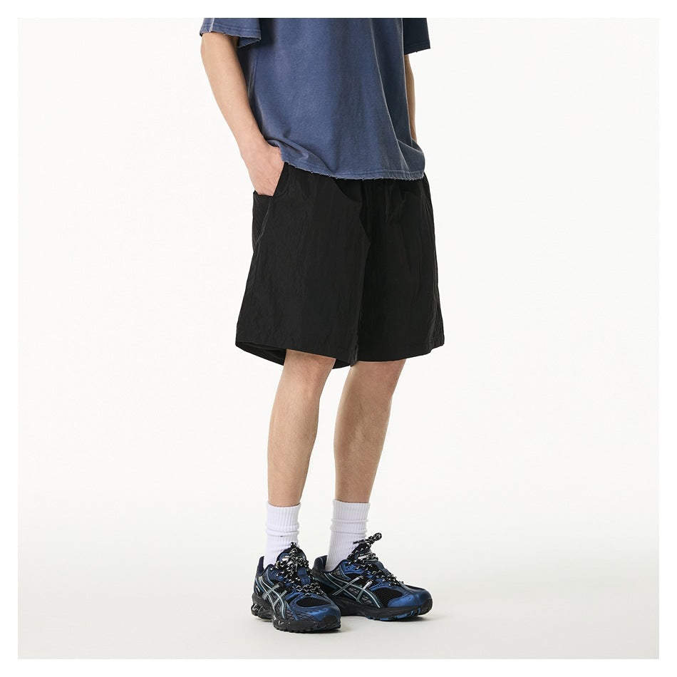 Side-angled view of a model wearing loose black knee-length shorts with a drawstring and pockets.