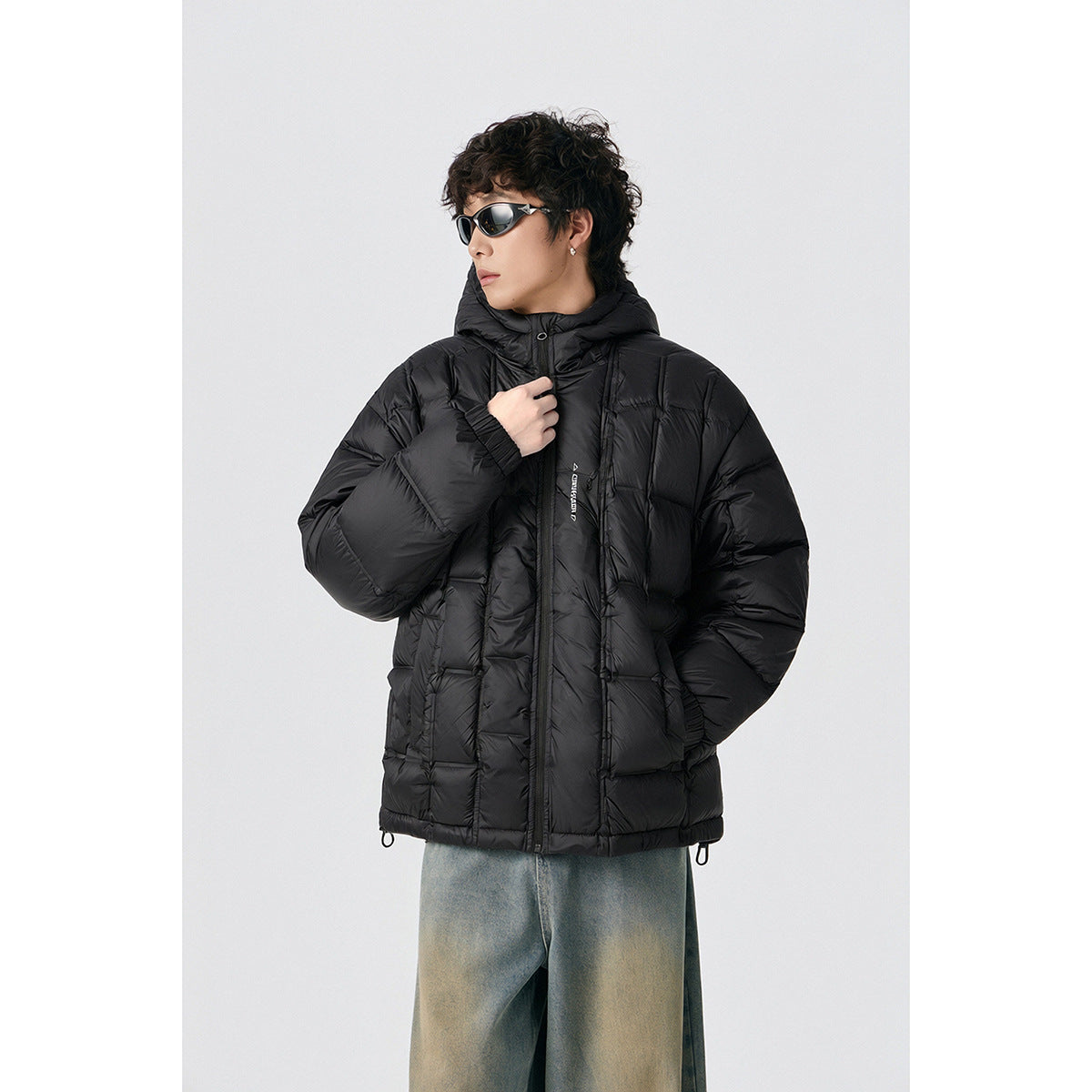 Closer view of a model wearing a black hooded puffer jacket with front pockets and a zipper.