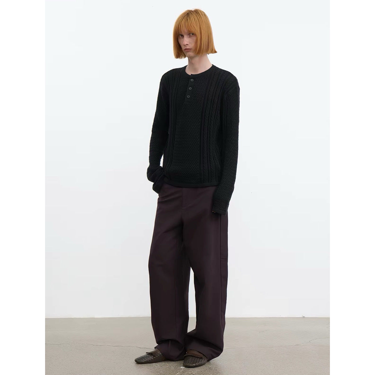 Model wearing a black textured knit pullover with a short button placket and dark wide-leg trousers.
