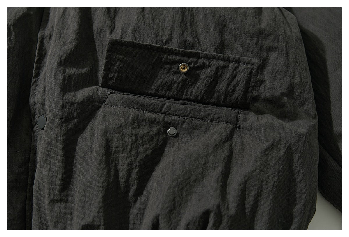 Close-up of a charcoal jacket pocket with a snap-fastened flap and visible metal snap hardware.