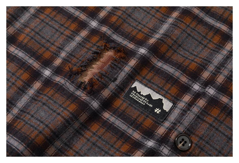 Close-up of a distressed hole and sewn patch on gray, rust, and black plaid fabric, with a dark button.