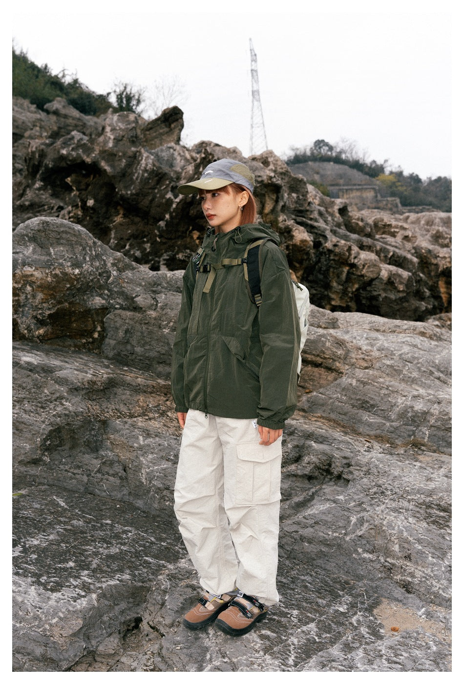 A woman in three-quarter view wears a dark green hooded jacket and off-white cargo pants outdoors.