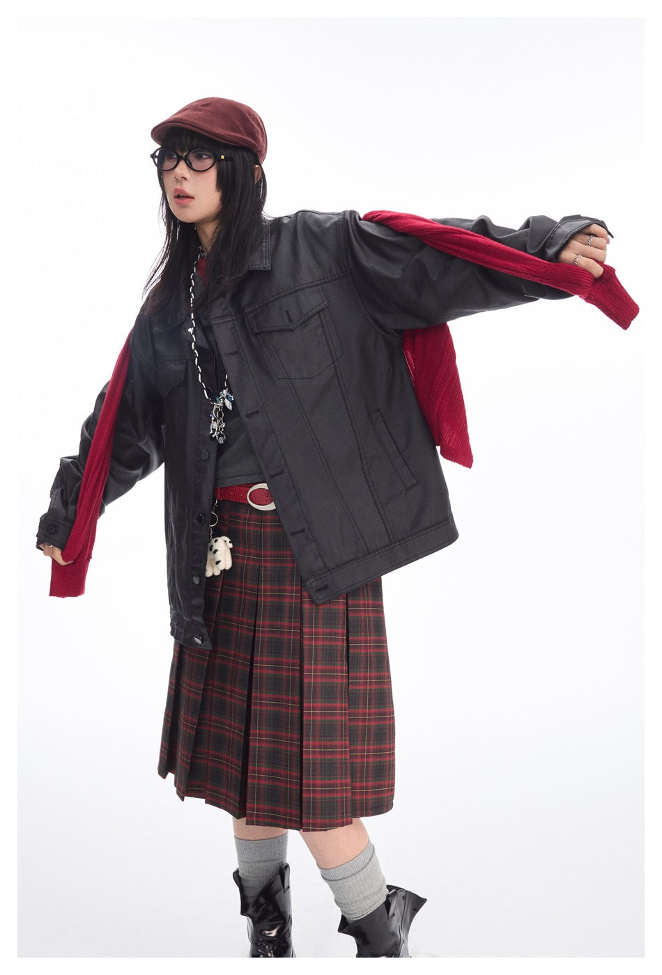 Model wearing an oversized black button-front jacket with flap pockets, shown with a red scarf and plaid skirt.