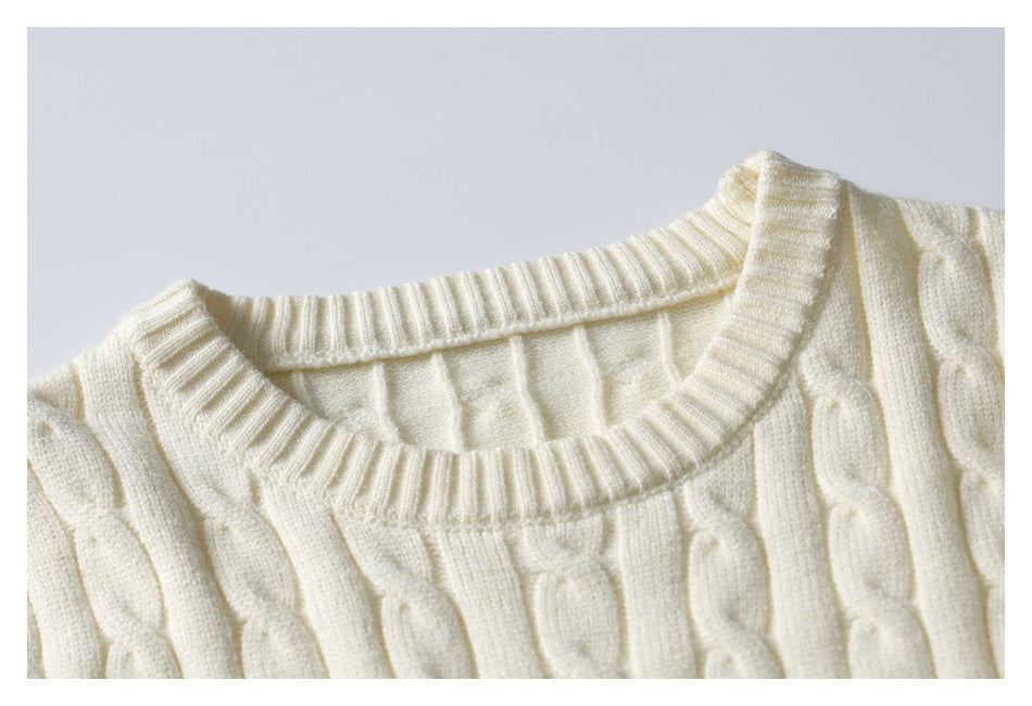 Close-up of an ivory cable-knit sweater's ribbed crew neckline and raised cable pattern.