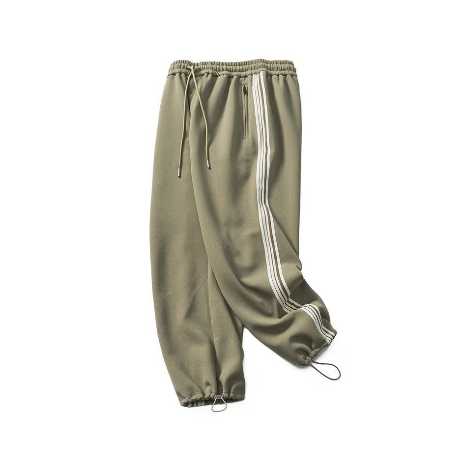 Front view of olive jogger pants with a drawstring waist, zip pocket, three cream side stripes and gathered cuffs.
