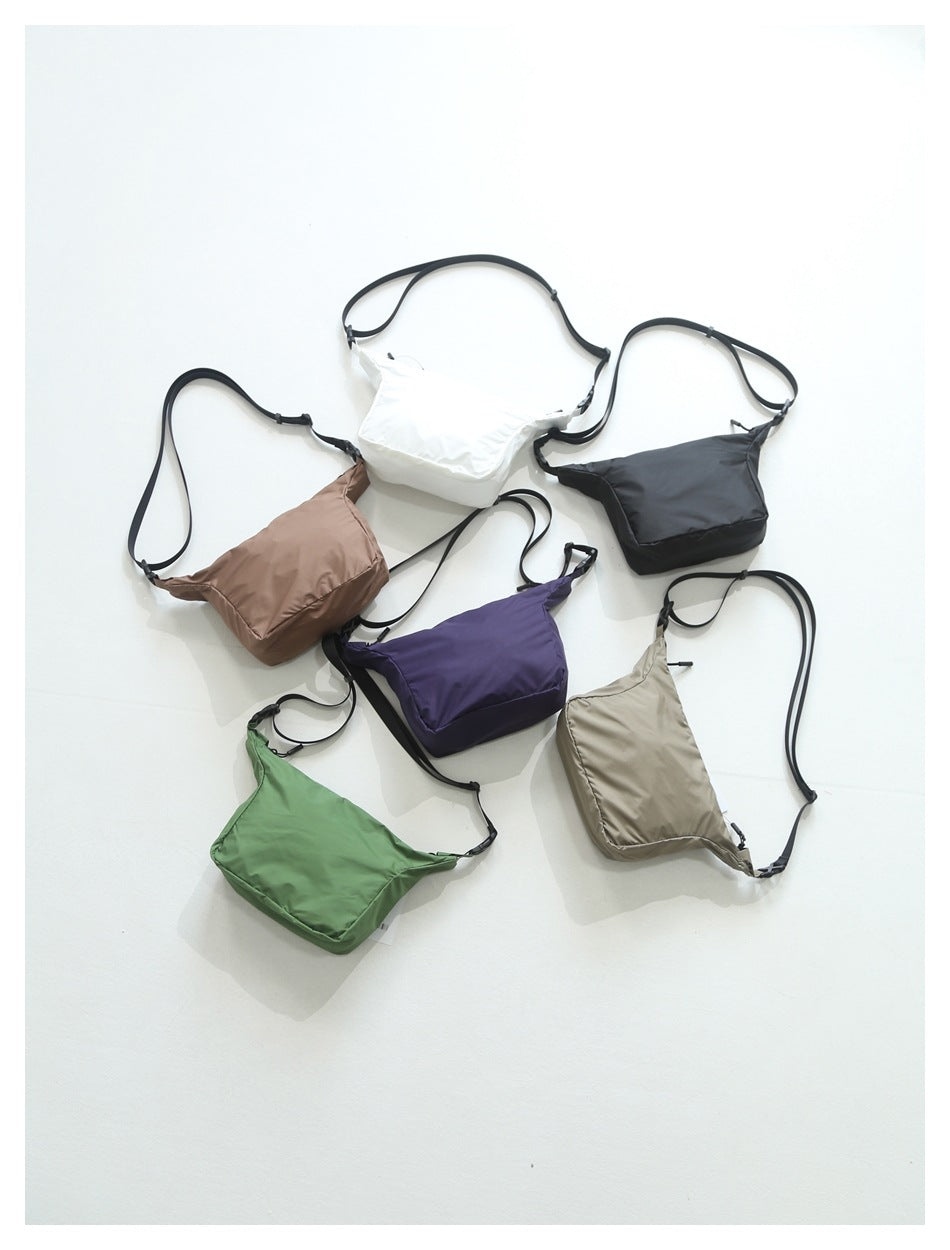 Six crossbody bags in brown, white, black, purple, green and khaki laid together on a light surface